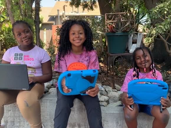 Three smiling girls sitting outside with tablets